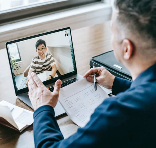 a white man with grey hair holding papers and pen and is in the video meeting with asian young man in glasses